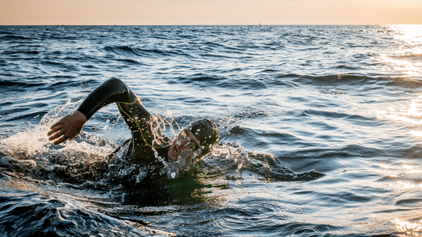 man swimming in ocean at sunrise
